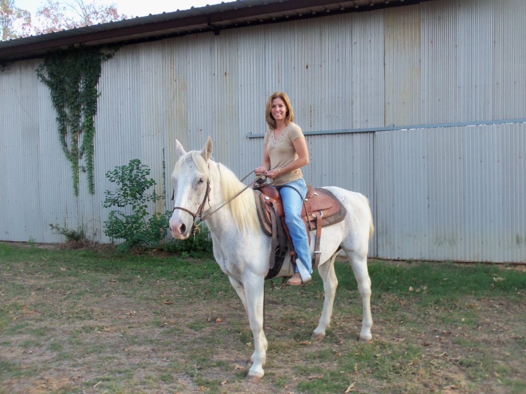 Lesha riding a white horse in front of the stables